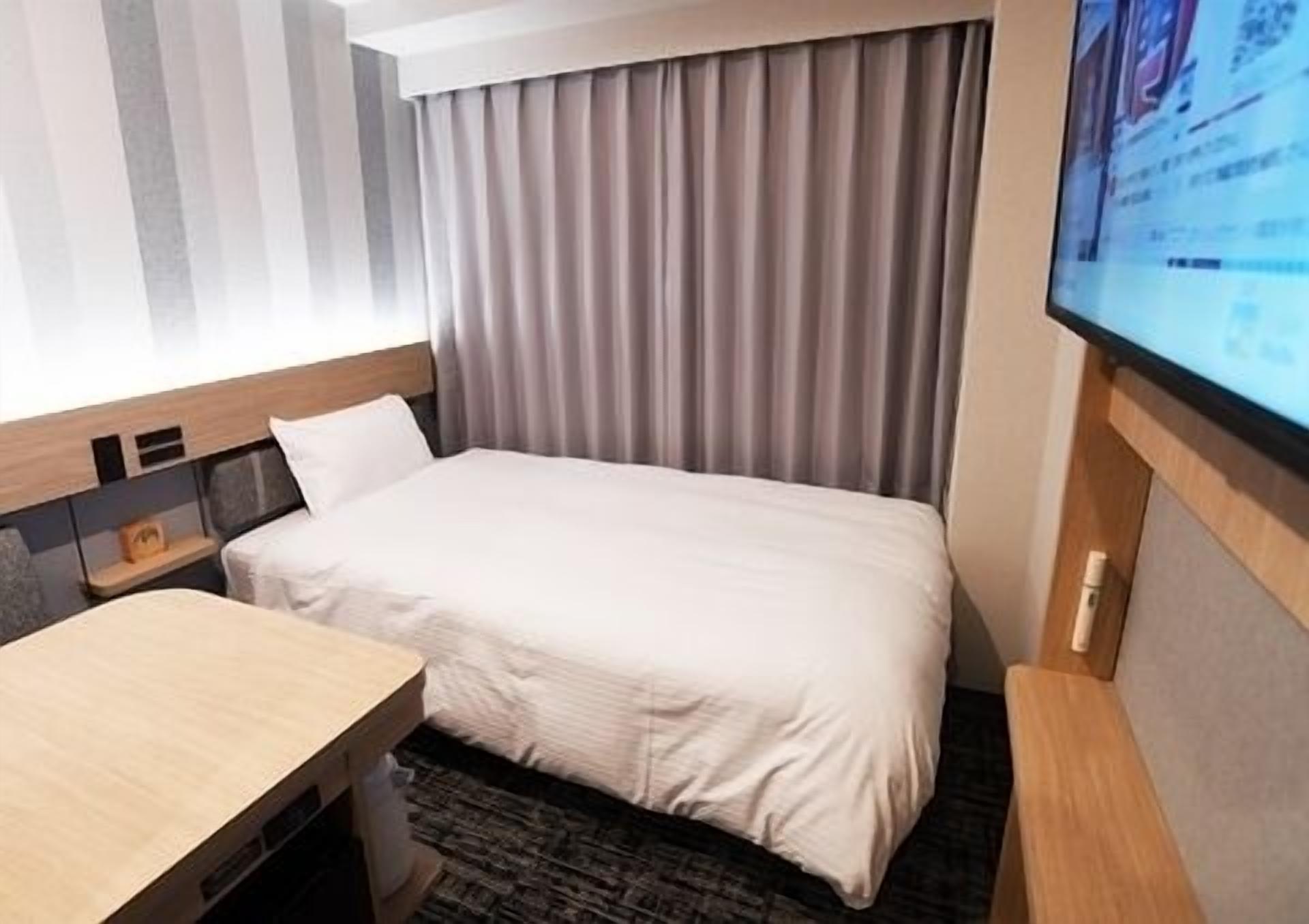 Une chambre d’hôtel avec un lit, un bureau, une télévision et une fenêtre avec des rideaux.