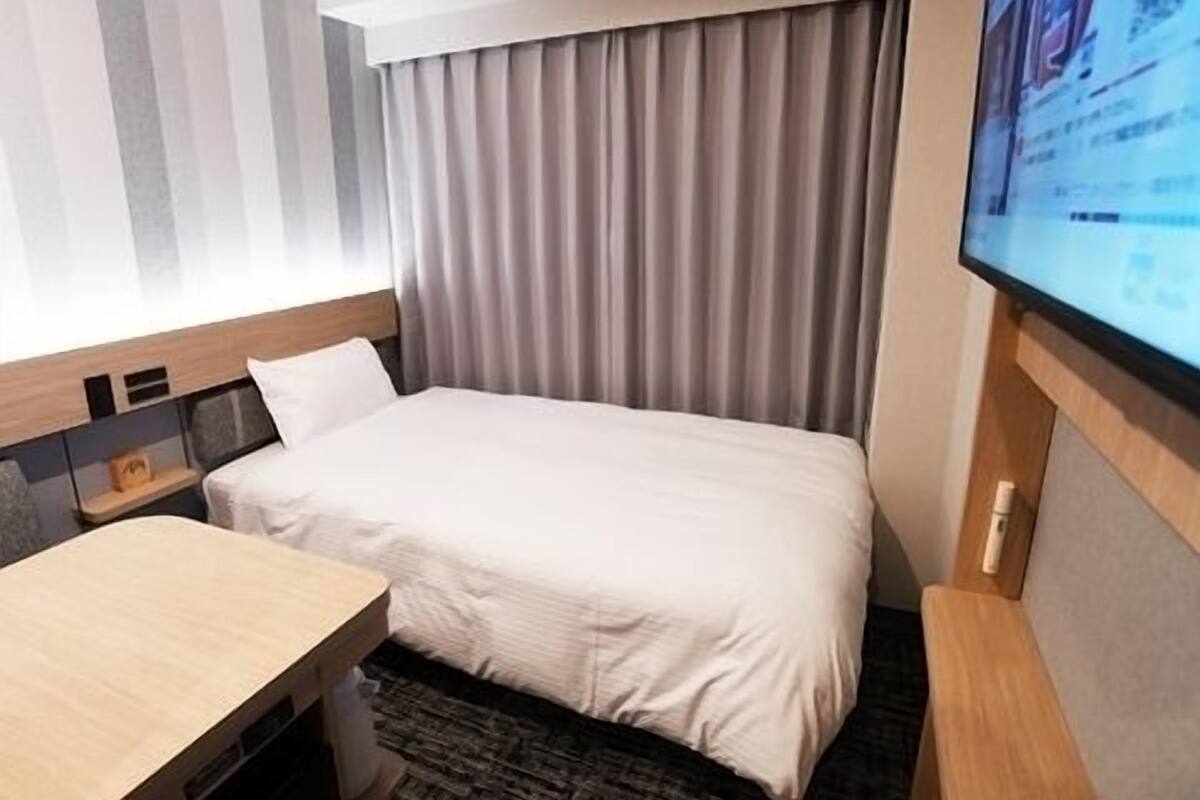 A hotel room with a bed, a desk, a television, and a window with curtains.