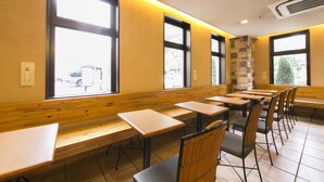 A restaurant with wooden tables and chairs, large windows, and a stone accent wall.