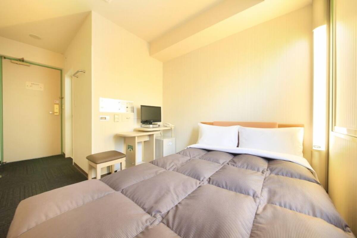 A hotel room with a bed, a desk with a computer, a chair, and a door.