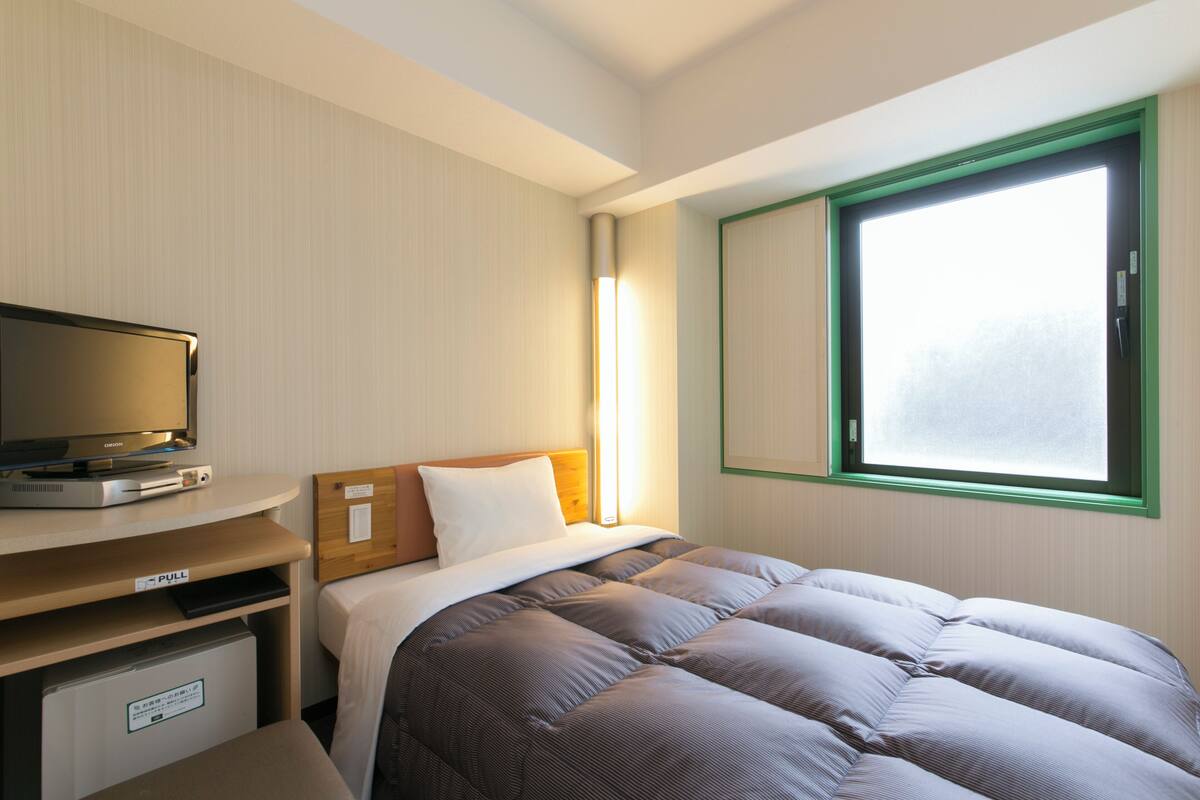 Une chambre d’hôtel comprenant un lit, un bureau escamotable avec un téléviseur, une fenêtre donnant sur un paysage agréable et une lampe de chevet.