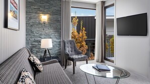 A modern living room with a stone wall, a grey armchair, a glass coffee table, and a mounted TV. - DoubleTree by Hilton Queenstown (Kawarau Falls)