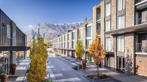 A modern building with stone facades and large windows, a clear sky, and a mountain in the background. - DoubleTree by Hilton Queenstown (Kawarau Falls)