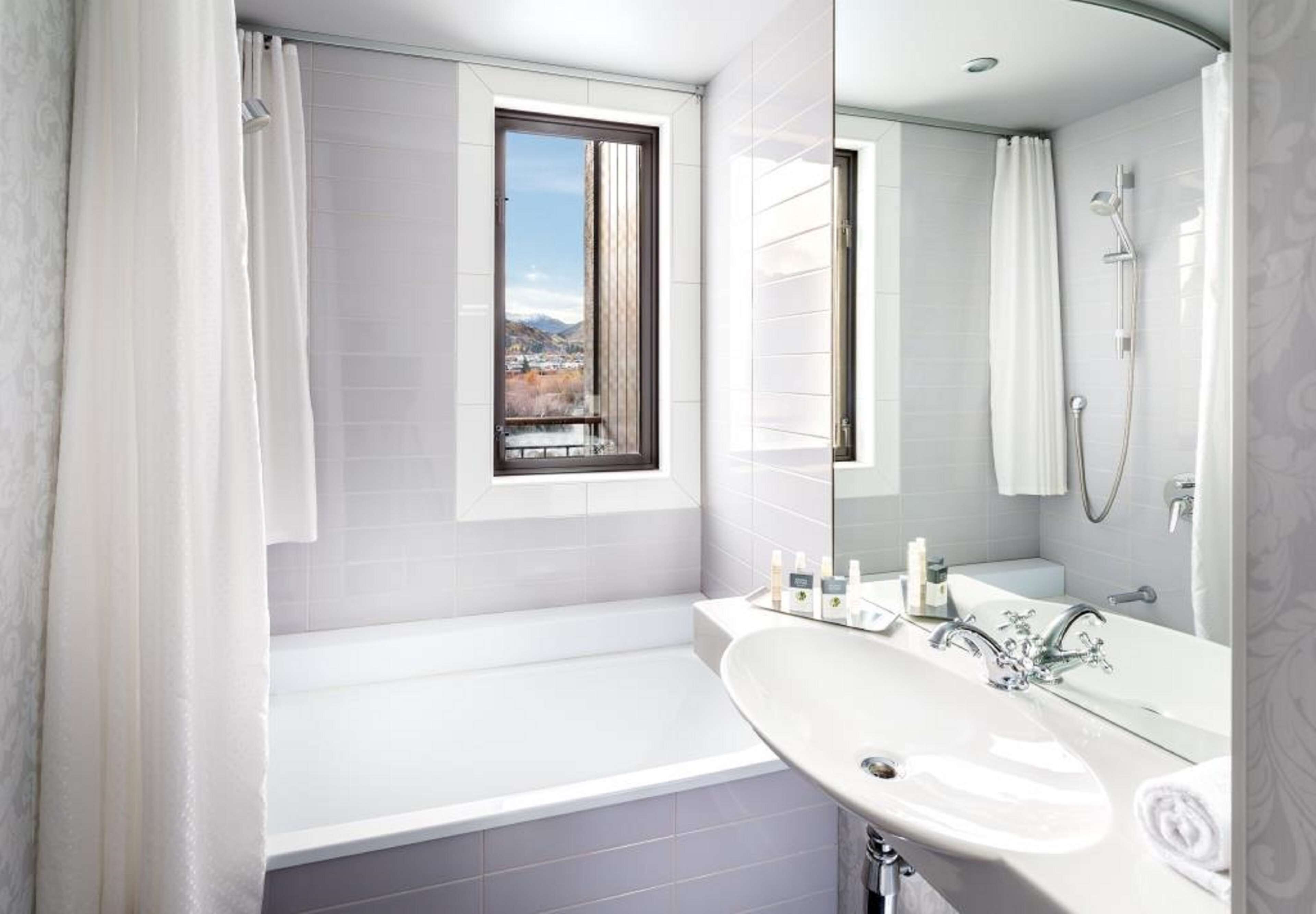 A modern bathroom with a bathtub, a sink, and a shower. There is a window above the bathtub and a mirror above the sink.