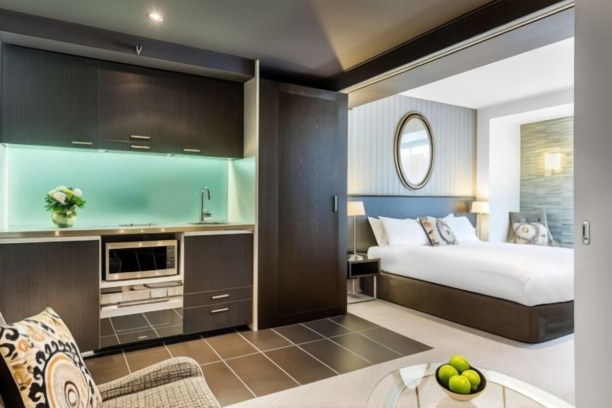 Una habitación de hotel moderna con una kitchenette separada, una cama grande y un espejo redondo sobre la cama.