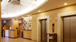 A hotel lobby with a reception desk, a coffee machine, an elevator, and a wall with directional signs.
