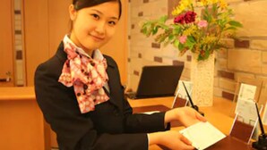 Un espace d’accueil avec un bureau, un ordinateur portable, un vase de fleurs et une personne tenant une carte.
