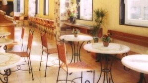 Un hall d’hôtel avec une longue rangée de tables et de chaises, de grandes fenêtres et un motif à carreaux sur le sol.