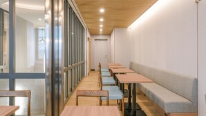 A modern interior with long tables and benches, a wooden ceiling, and a glass partition.