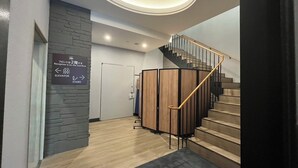 A modern hotel lobby with a reception desk, a staircase, and a sign indicating the reception is on the second floor.