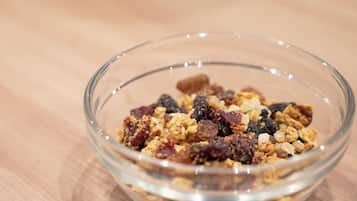 A clear glass bowl containing a mix of granola and dried fruits on a wooden surface.