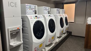 A row of white commercial washing machines with control panels, a water dispenser, and a door with a window.