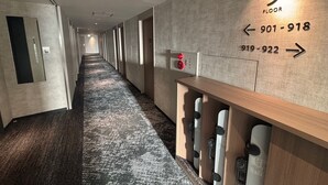 A hotel corridor with a wooden bench, a wall-mounted number sign indicating floor 9, and directional arrows with phone numbers.