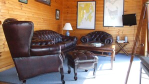A wooden-paneled room with a leather sofa, a matching ottoman, and a small table with a lamp. There are framed pictures and a map on the walls. - Bruny Island Escapes and Hotel Bruny (Alonnah)