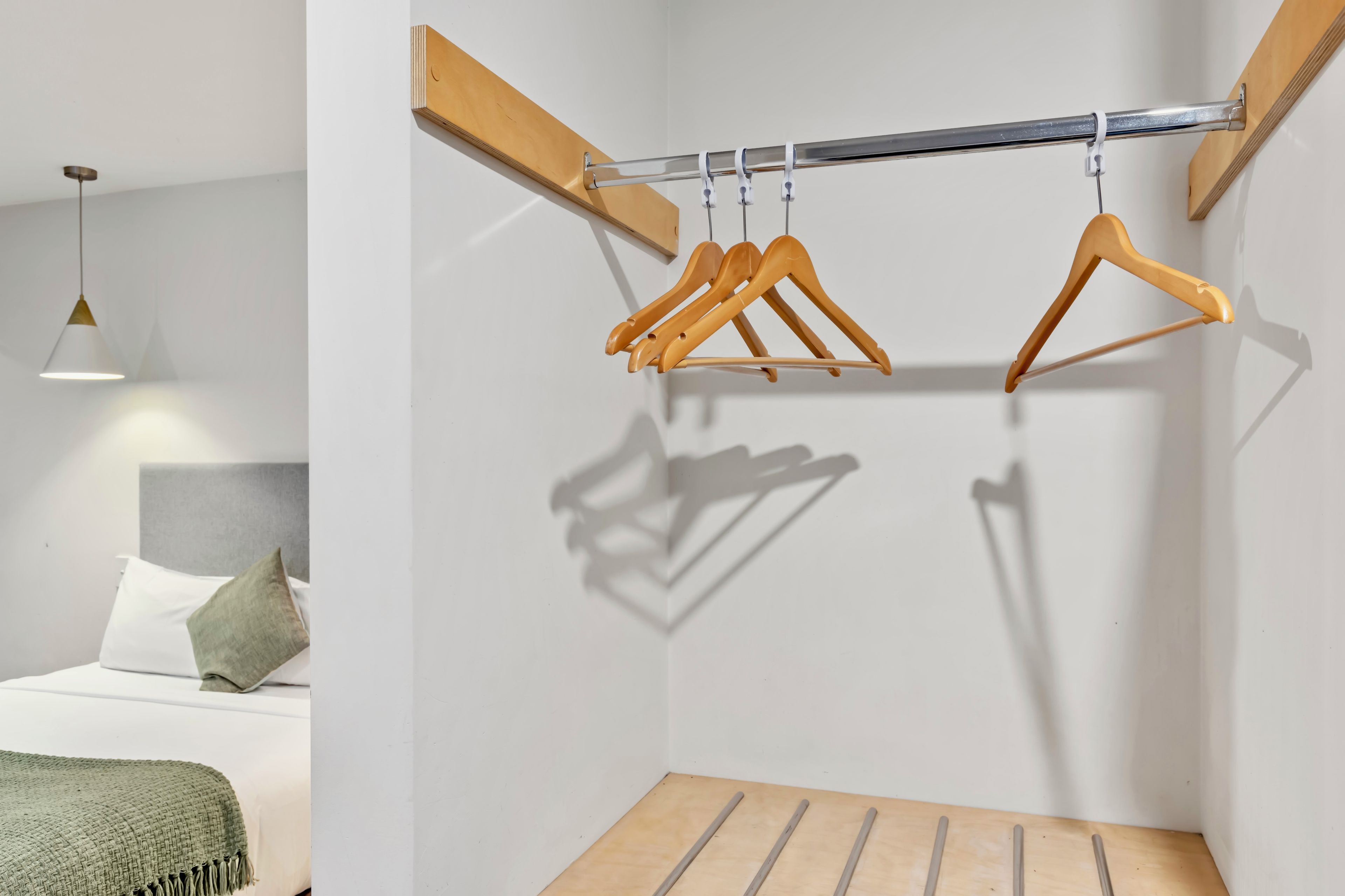 Una habitación minimalista con una cama, un perchero de madera colgante y una lámpara colgante.