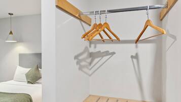 Una habitación minimalista con una cama, un perchero de madera colgante y una lámpara colgante.