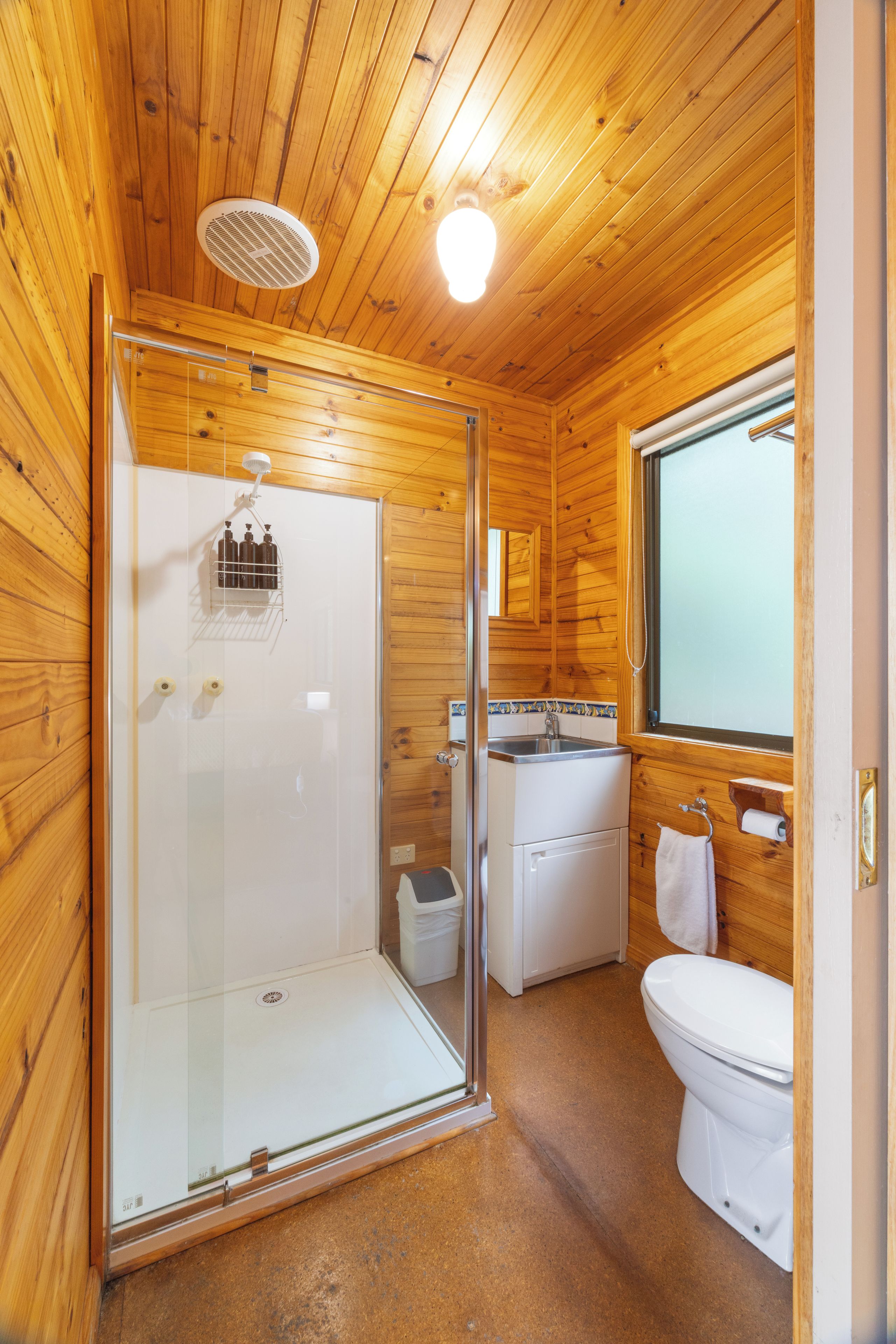 A compact wooden cabin bathroom with a glass-enclosed shower, a sink, and a toilet.