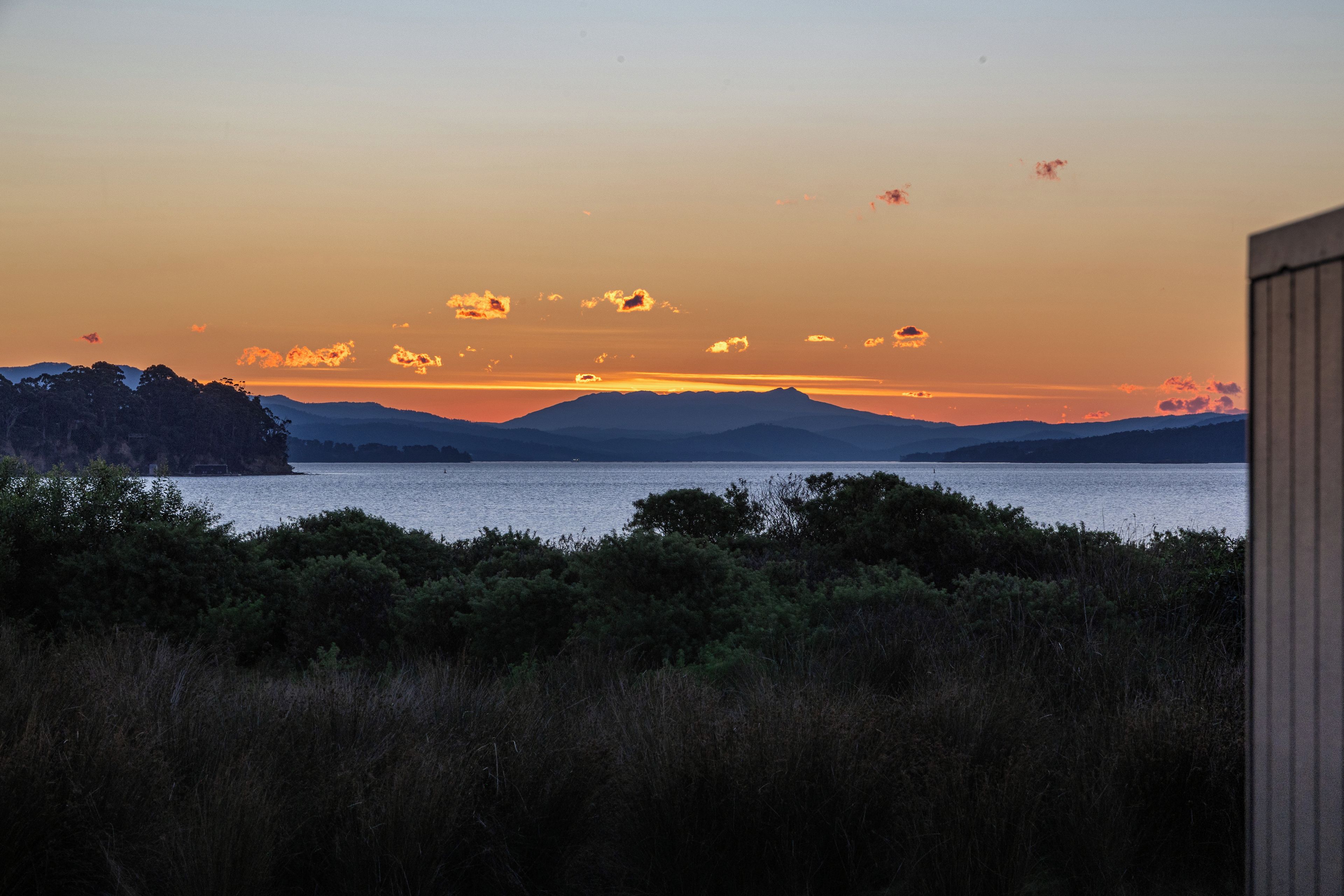 Eine Küstenlandschaft mit Blick auf das Meer und ferne Berge im Abendrot.