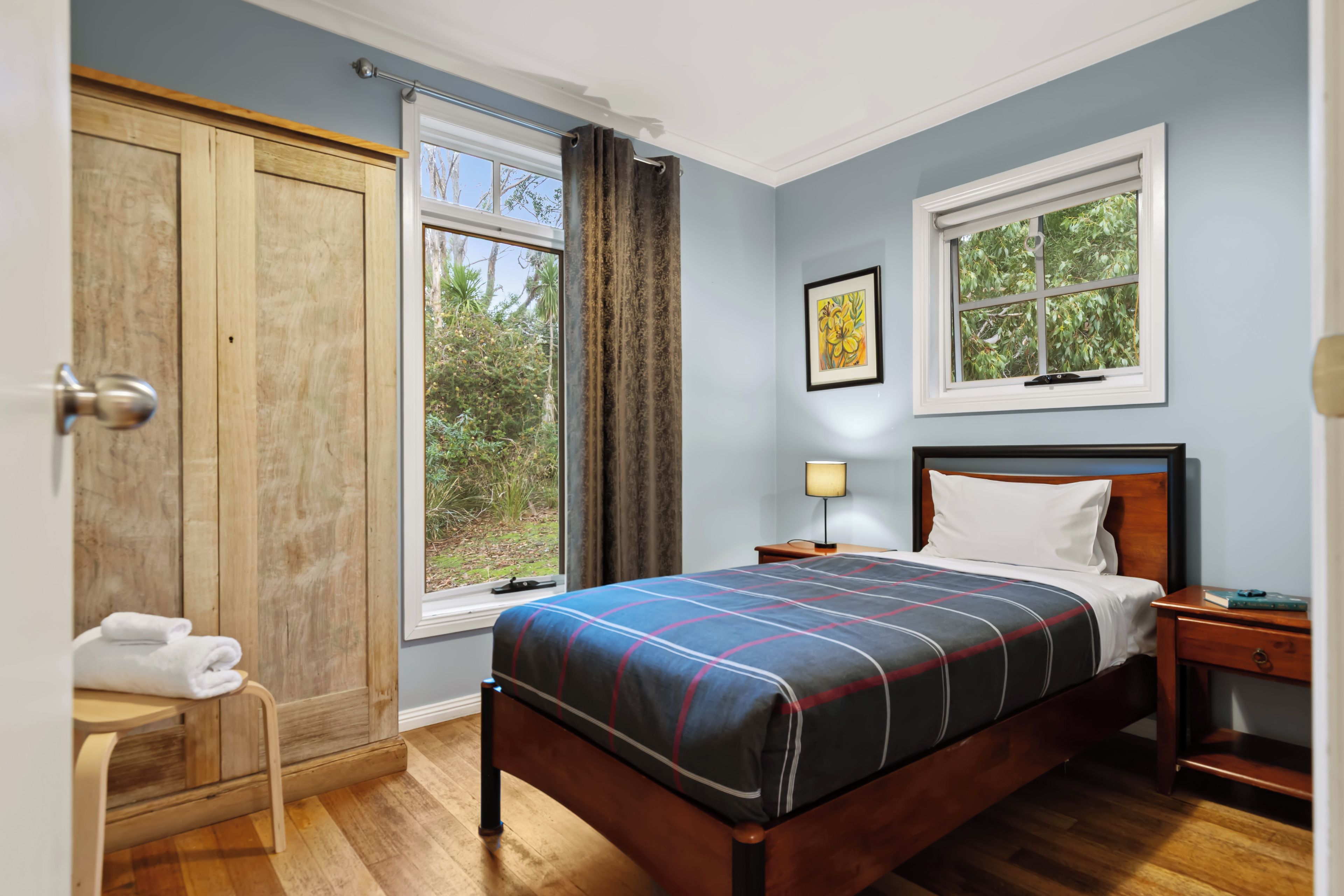 A bedroom with a wooden bed, a nightstand, a bedside lamp, a window with curtains, and a wardrobe.