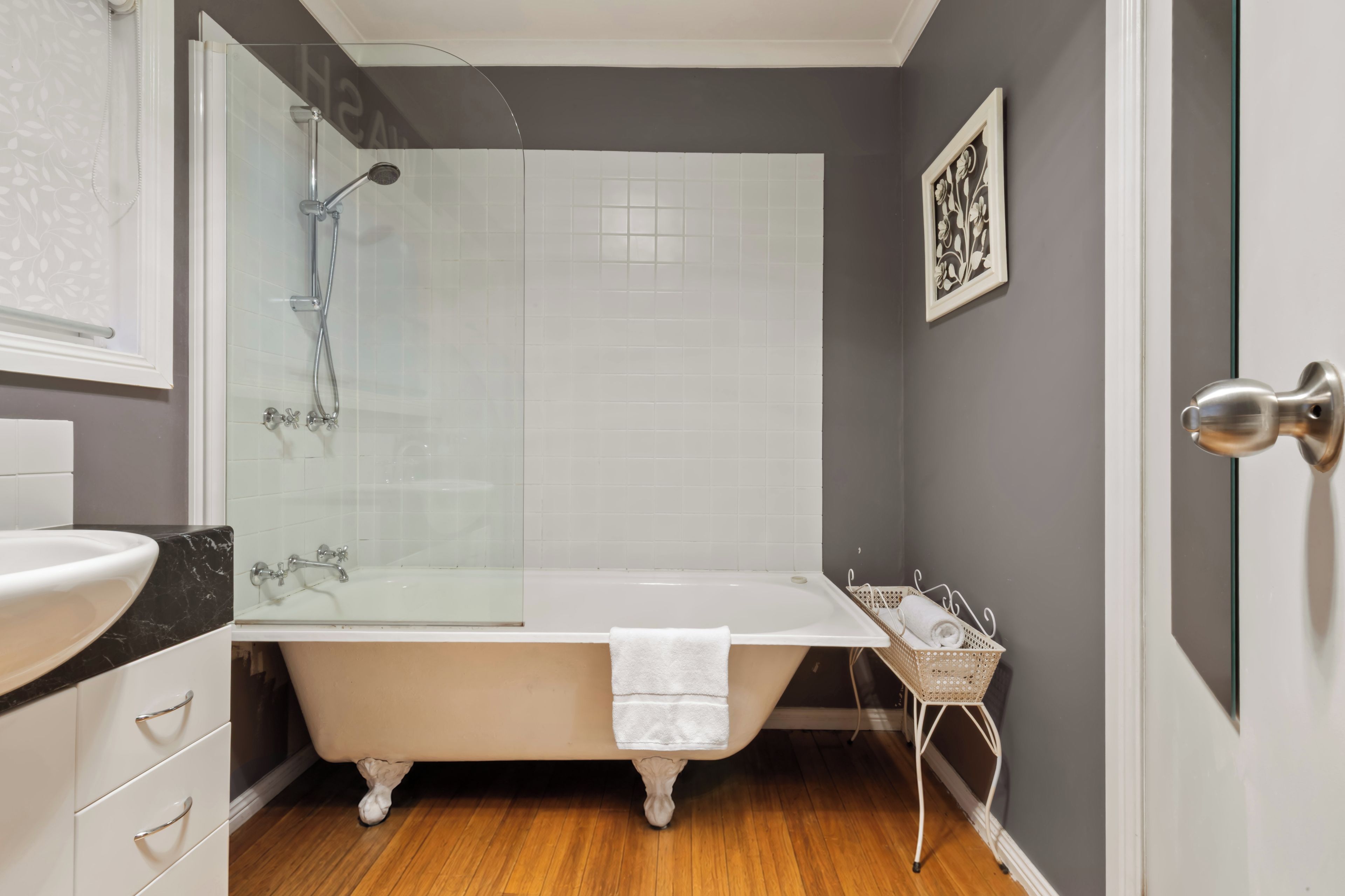A bathroom with a freestanding bathtub, a glass shower enclosure, a white sink, and a framed artwork on the wall.