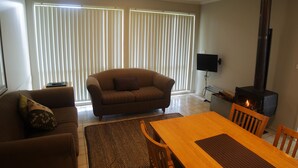 A living room with a sofa, a wooden dining table, and a fireplace. - Bruny Island Escapes and Hotel Bruny (Alonnah)
