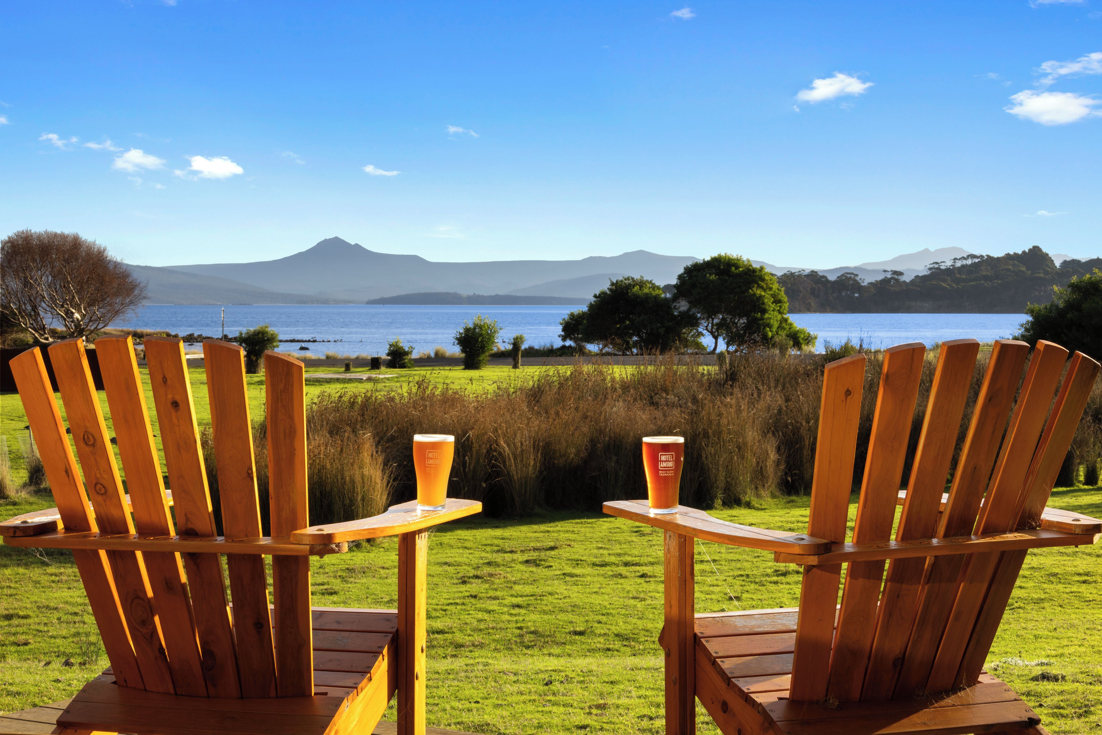 Twee houten Adirondack-stoelen gericht op een waterpartij, met een berg op de achtergrond.