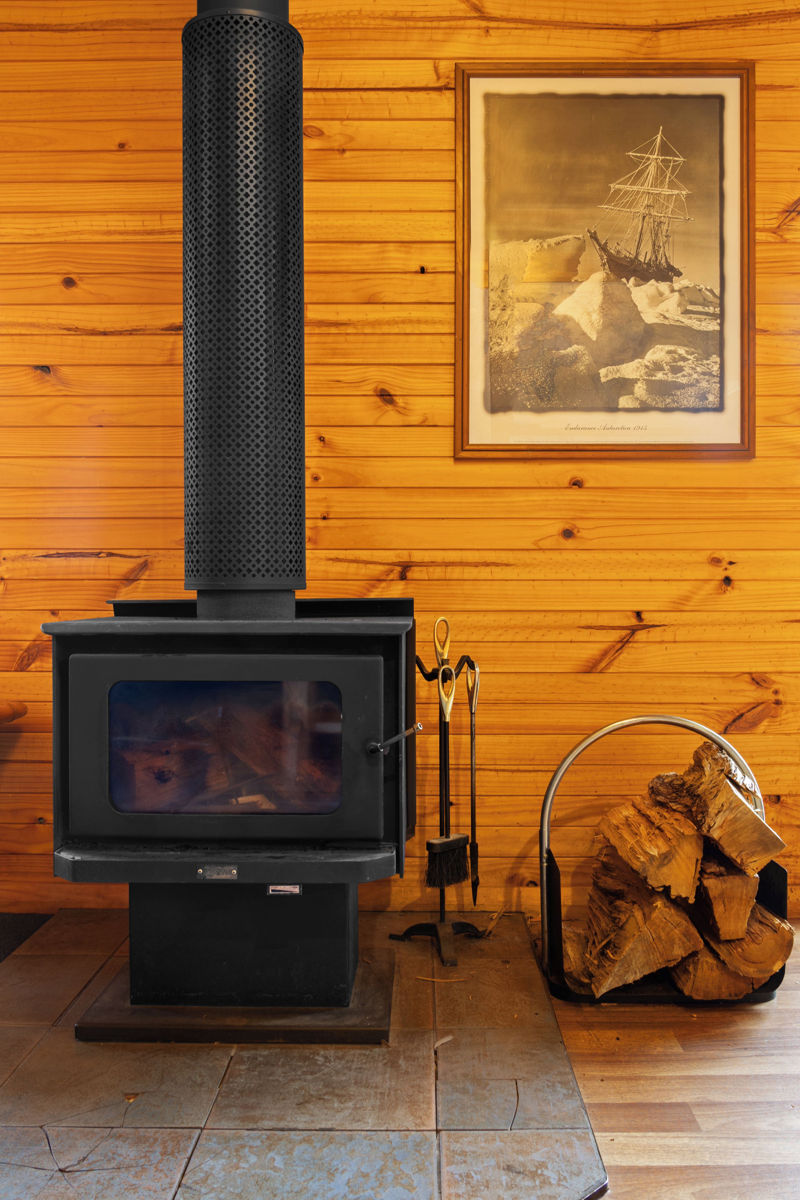 Una estufa de leña con chimenea, un cuadro en la pared y una pila de leña.