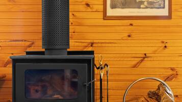 Una estufa de leña con chimenea, un cuadro en la pared y una pila de leña.