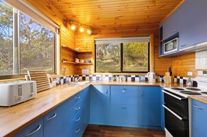 Una cocina compacta con armarios de madera, microondas, estufa y ventana con vistas a un paisaje natural.
