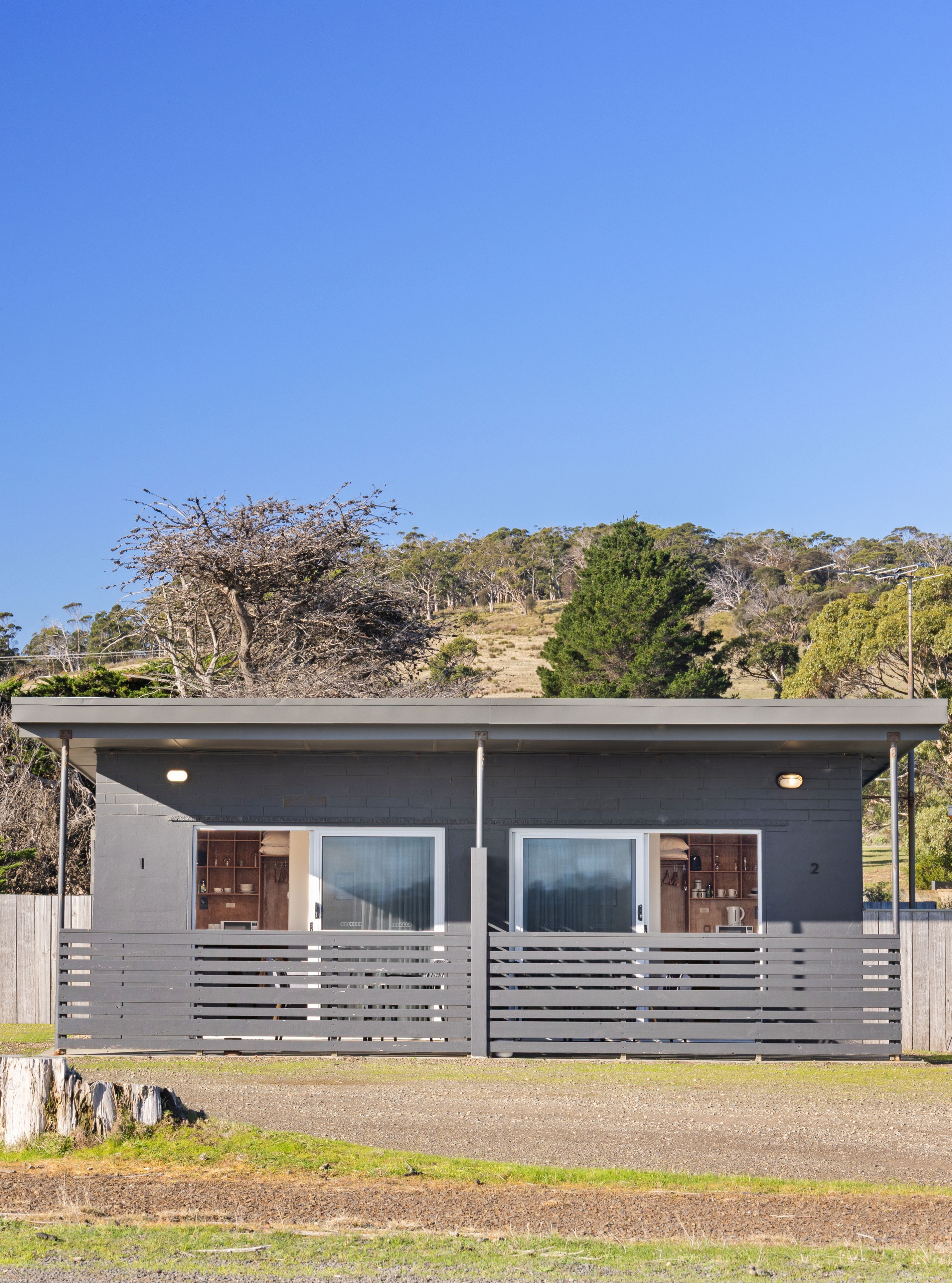 A two-story cabin with a balcony, large windows, and a view of the surrounding landscape.