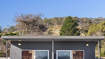 A two-story cabin with a balcony, large windows, and a view of the surrounding landscape.