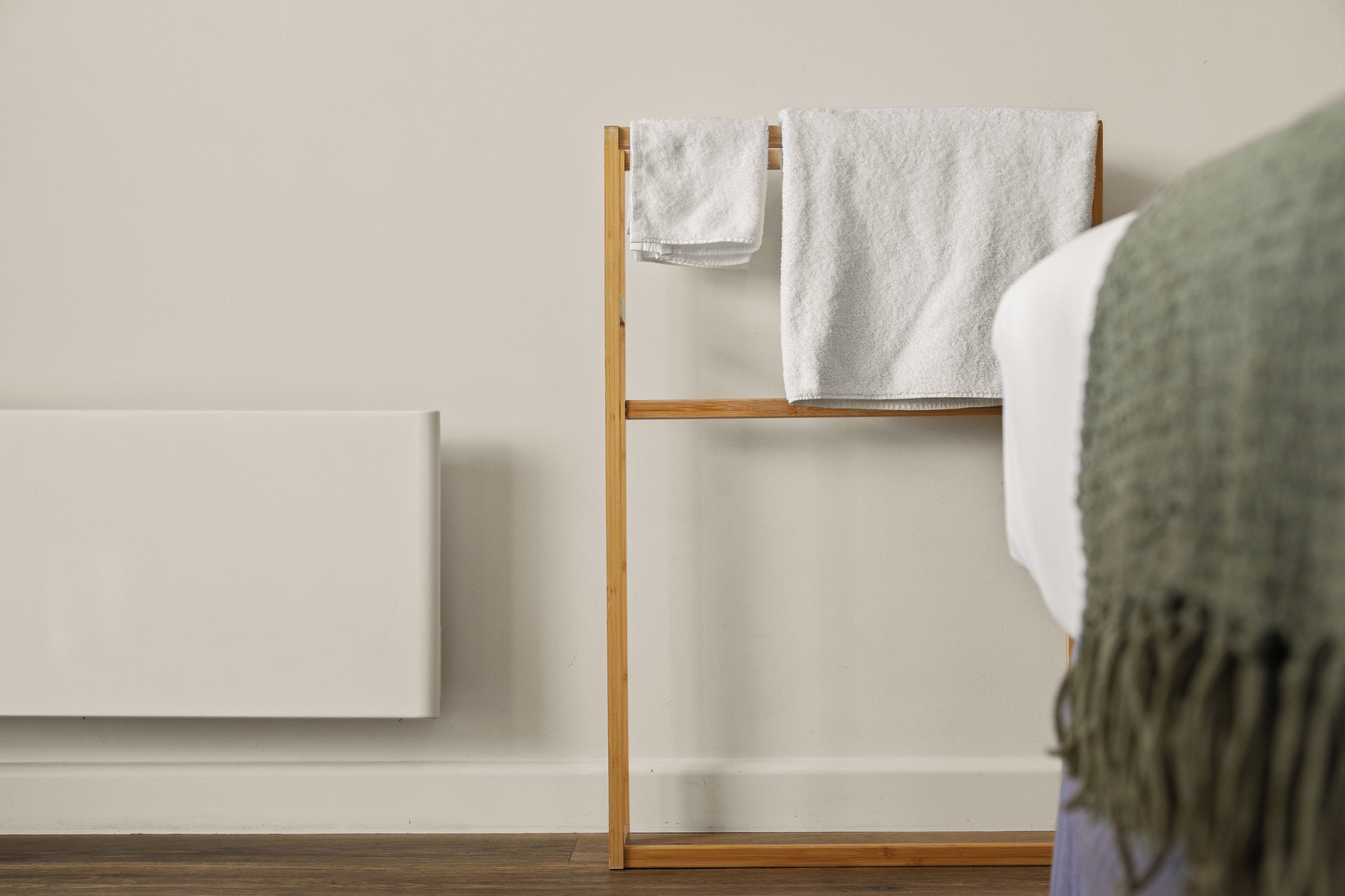 A room with a wooden drying rack holding two white towels, a white radiator, and a wooden floor.