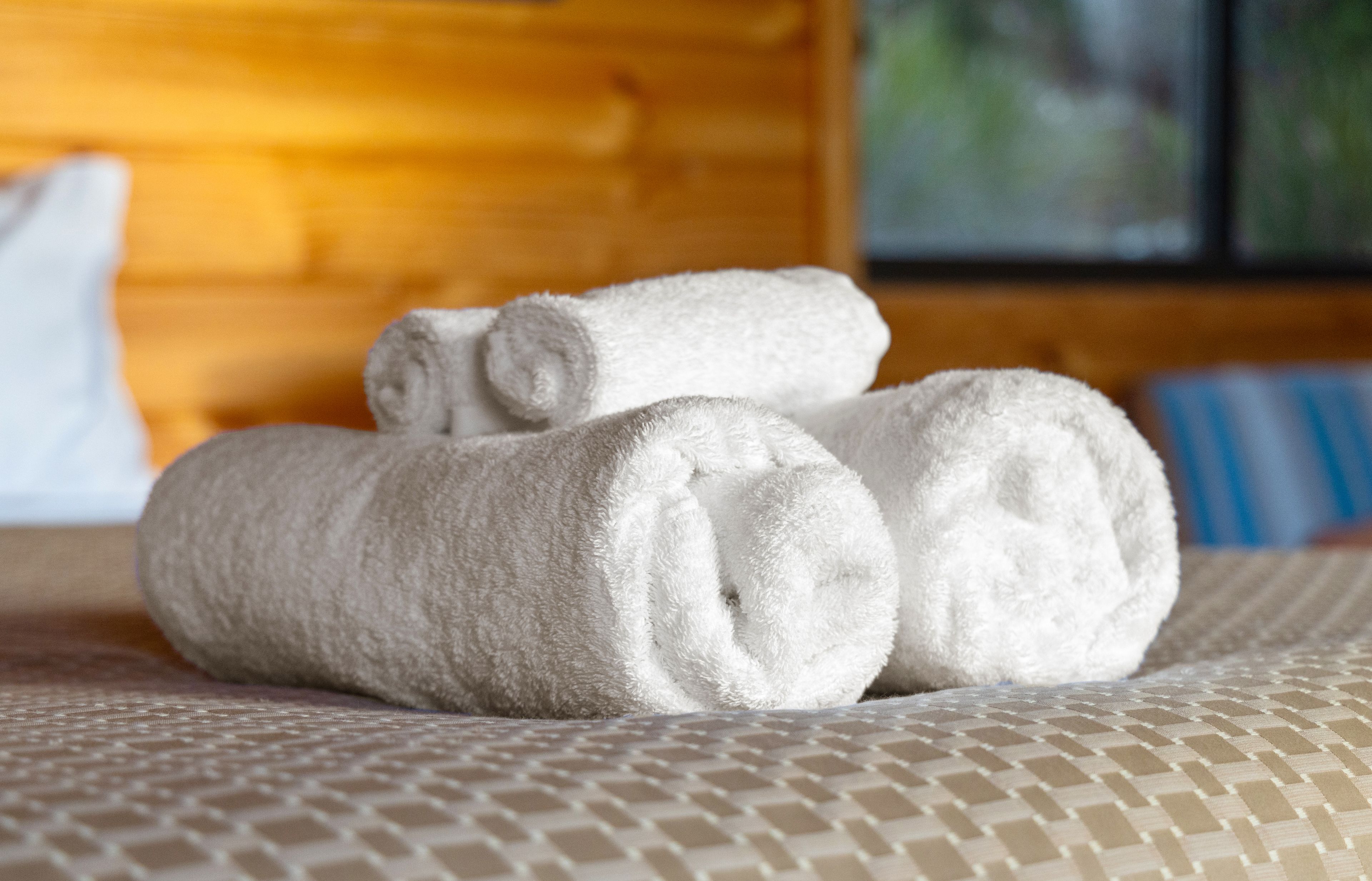 A bed with a patterned bedspread and rolled white towels.