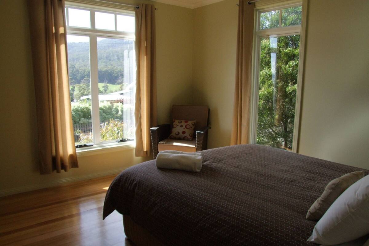 Une chambre avec un grand lit, une chaise et une fenêtre avec des rideaux.