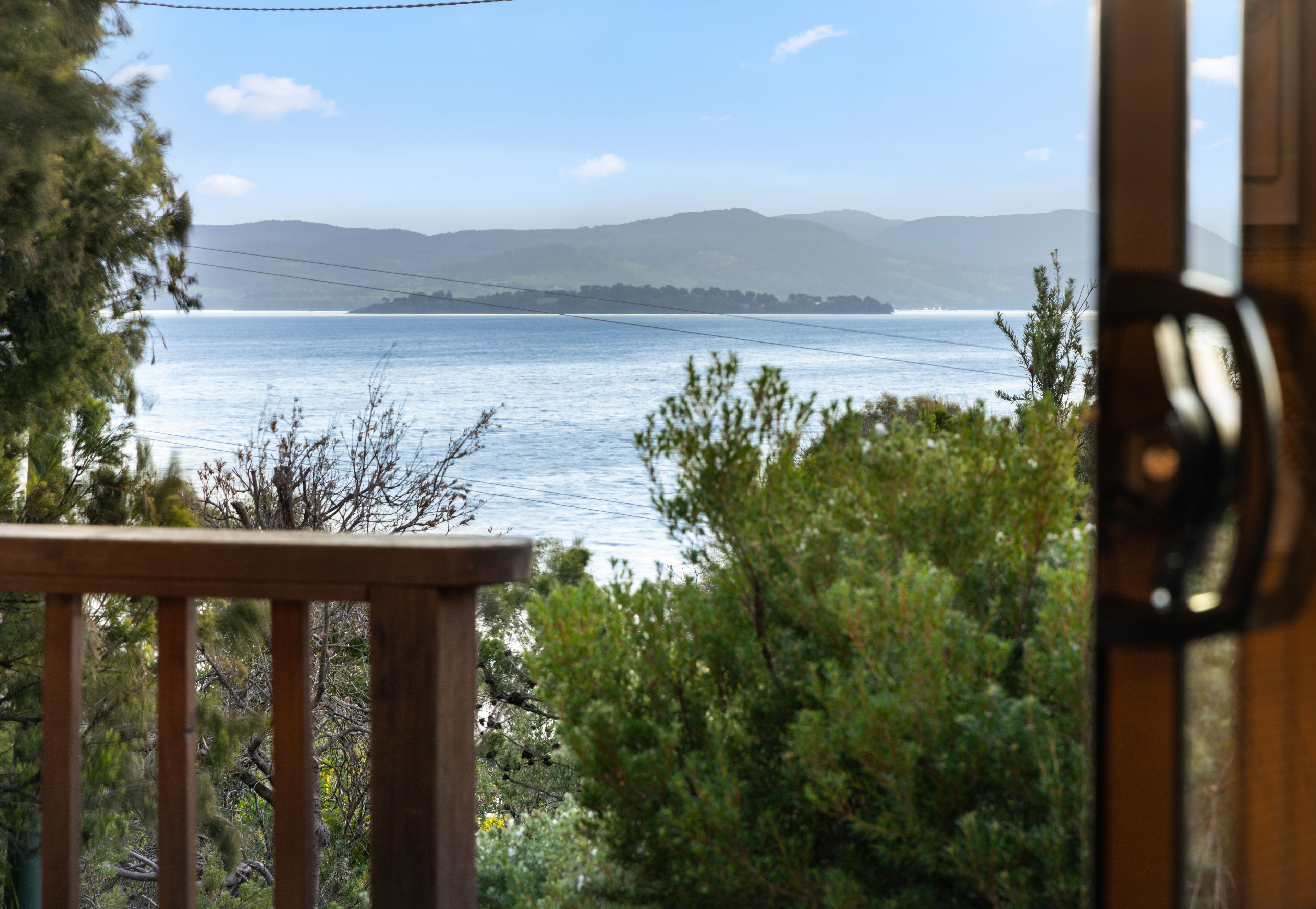 A view from a wooden deck overlooking a body of water with distant landforms and a clear sky.