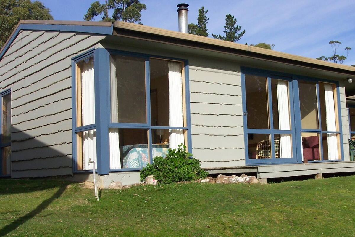 Une maison de plain-pied avec un toit à pignon, de grandes fenêtres et une cheminée.