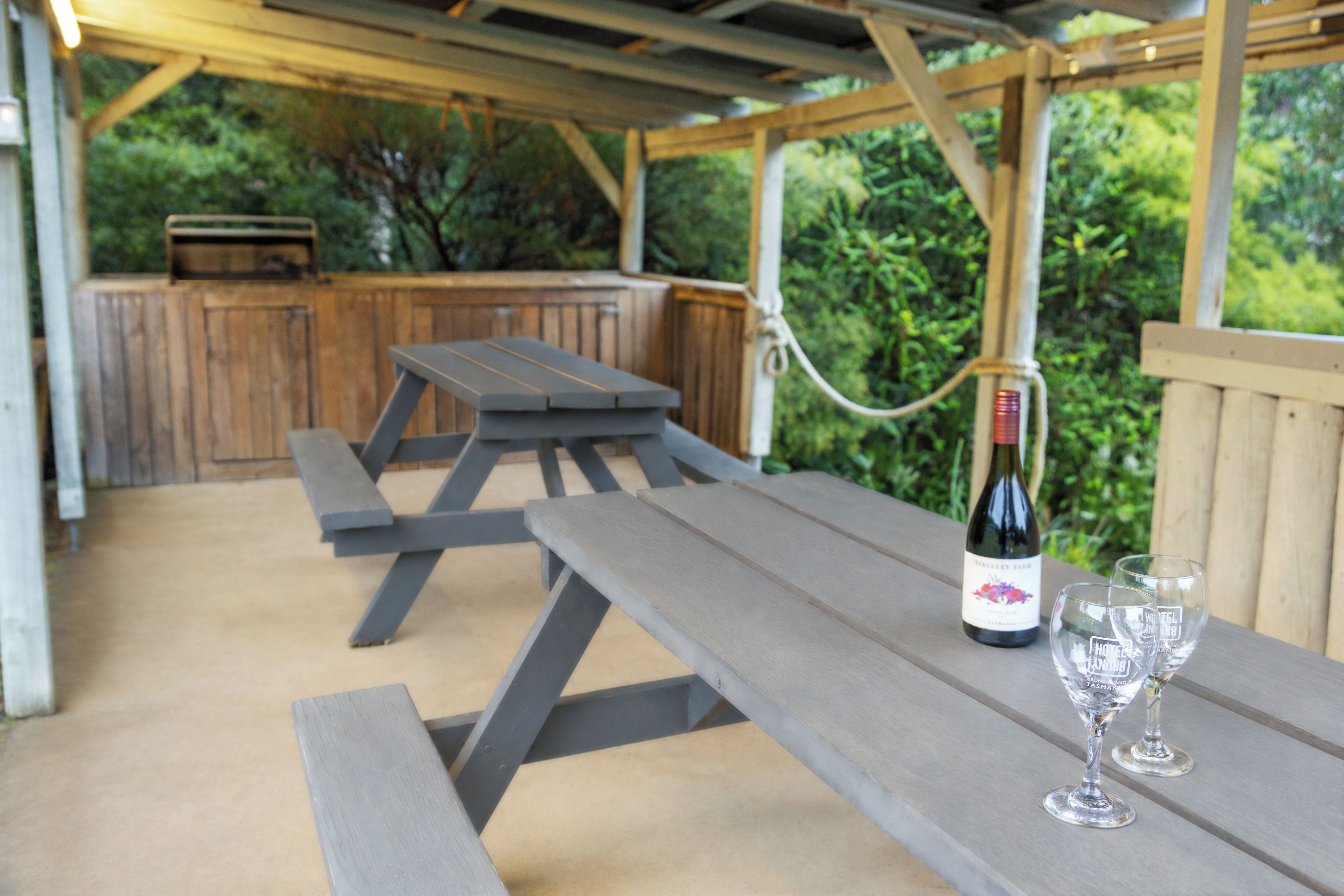 An outdoor patio with picnic tables and a wine bottle.
