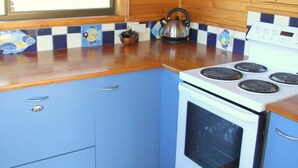 A kitchen with blue cabinets, a white stove, and a window with a curtain. - Bruny Island Escapes and Hotel Bruny (Alonnah)