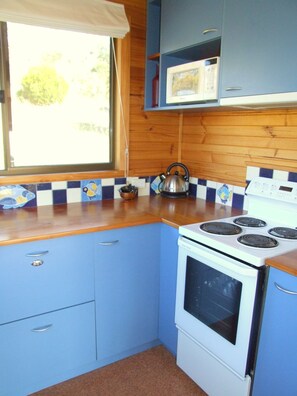 Una cocina con armarios azules, estufa blanca y una ventana con cortina.
