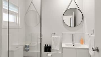 Un baño moderno con cabina de ducha de vidrio, inodoro, lavamanos con espejo y suelo de madera.