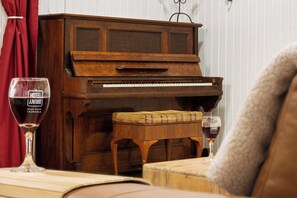 A wooden piano with a bench in front of it, a glass of red wine on a table, and a red curtain in the background. - Bruny Island Escapes and Hotel Bruny (Alonnah)