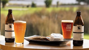 A table with two bottles of beer, a glass of beer, and a plate with cheese and crackers. - Bruny Island Escapes and Hotel Bruny (Alonnah)