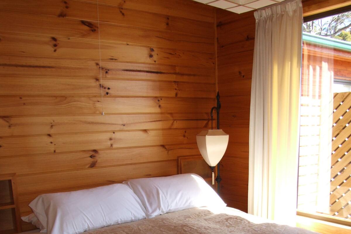 Une pièce aménagée comme un chalet en bois, avec un lit, une table de chevet et une lampe.