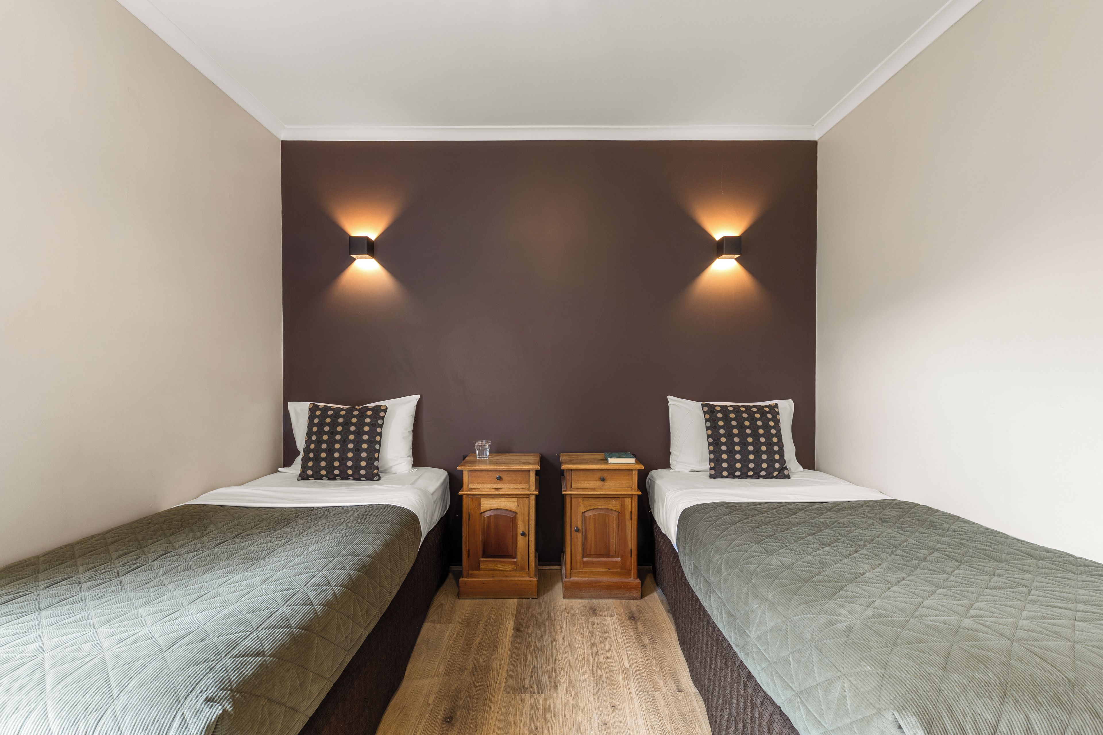Una habitación de hotel con dos camas individuales, una mesita de noche de madera y dos luces fijadas a la pared.