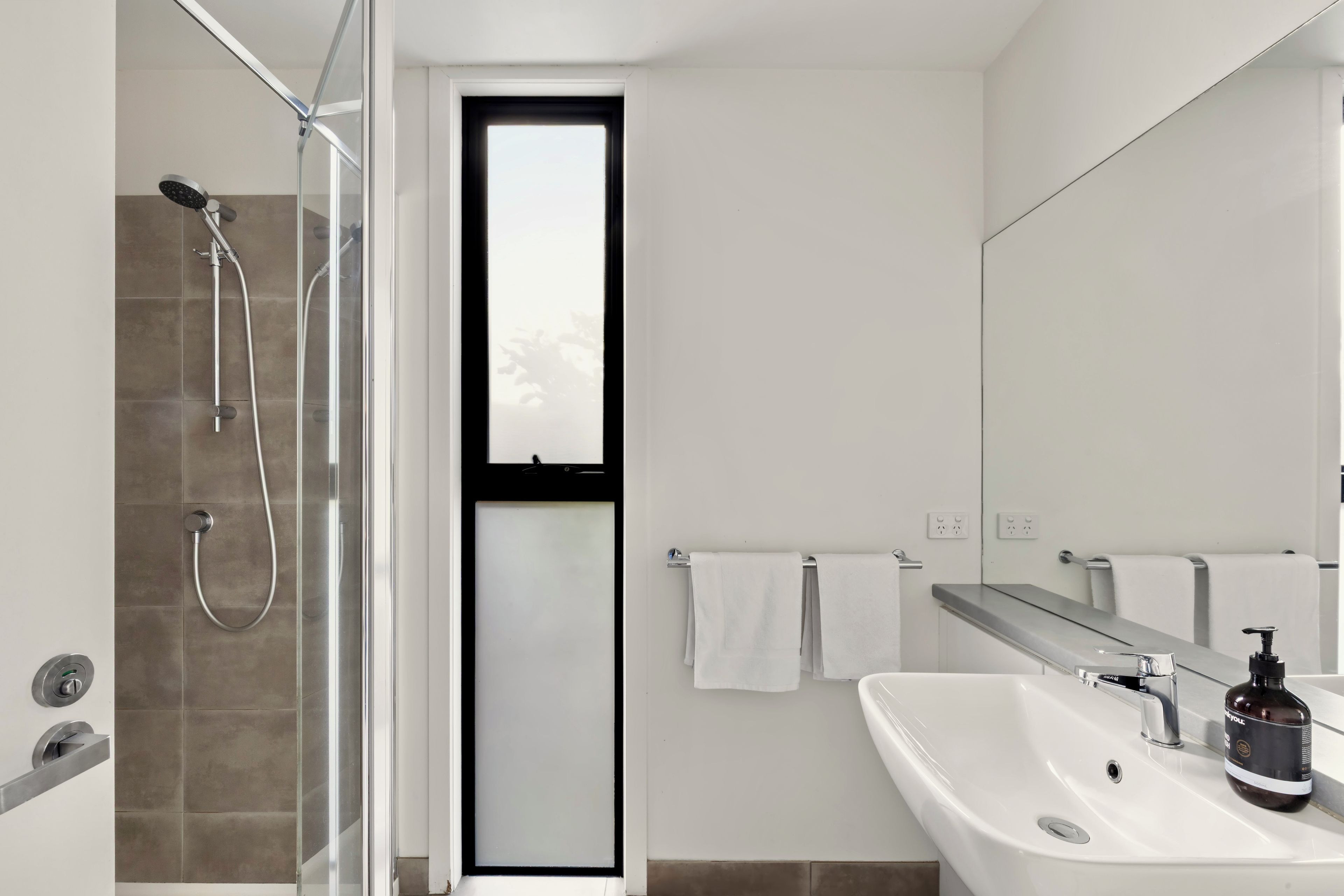 Un baño moderno con cabina de ducha de vidrio, un lavabo blanco y un espejo grande.