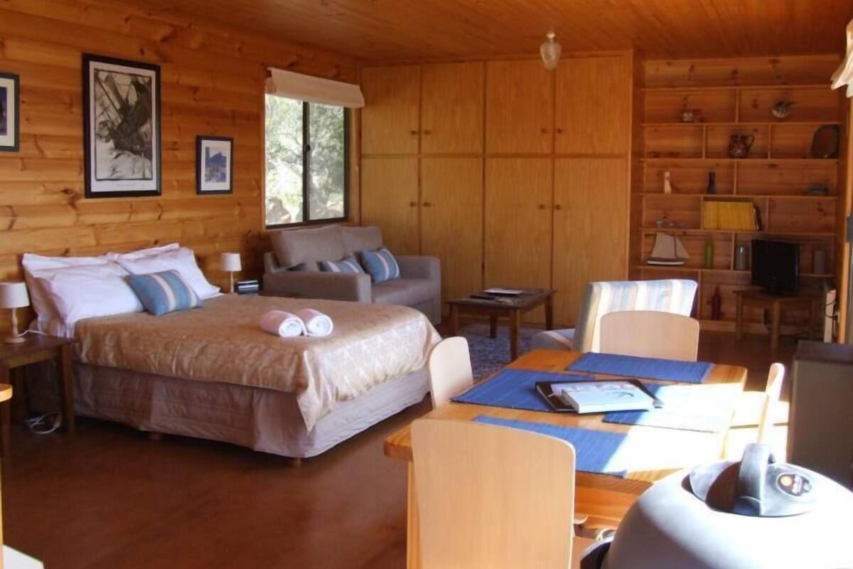 Une cabane en bois avec un lit, deux chaises, une table et un téléviseur.