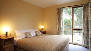 A bedroom with a large bed, two bedside lamps, a window with curtains, and a view of trees. - Bruny Island Escapes and Hotel Bruny (Alonnah)