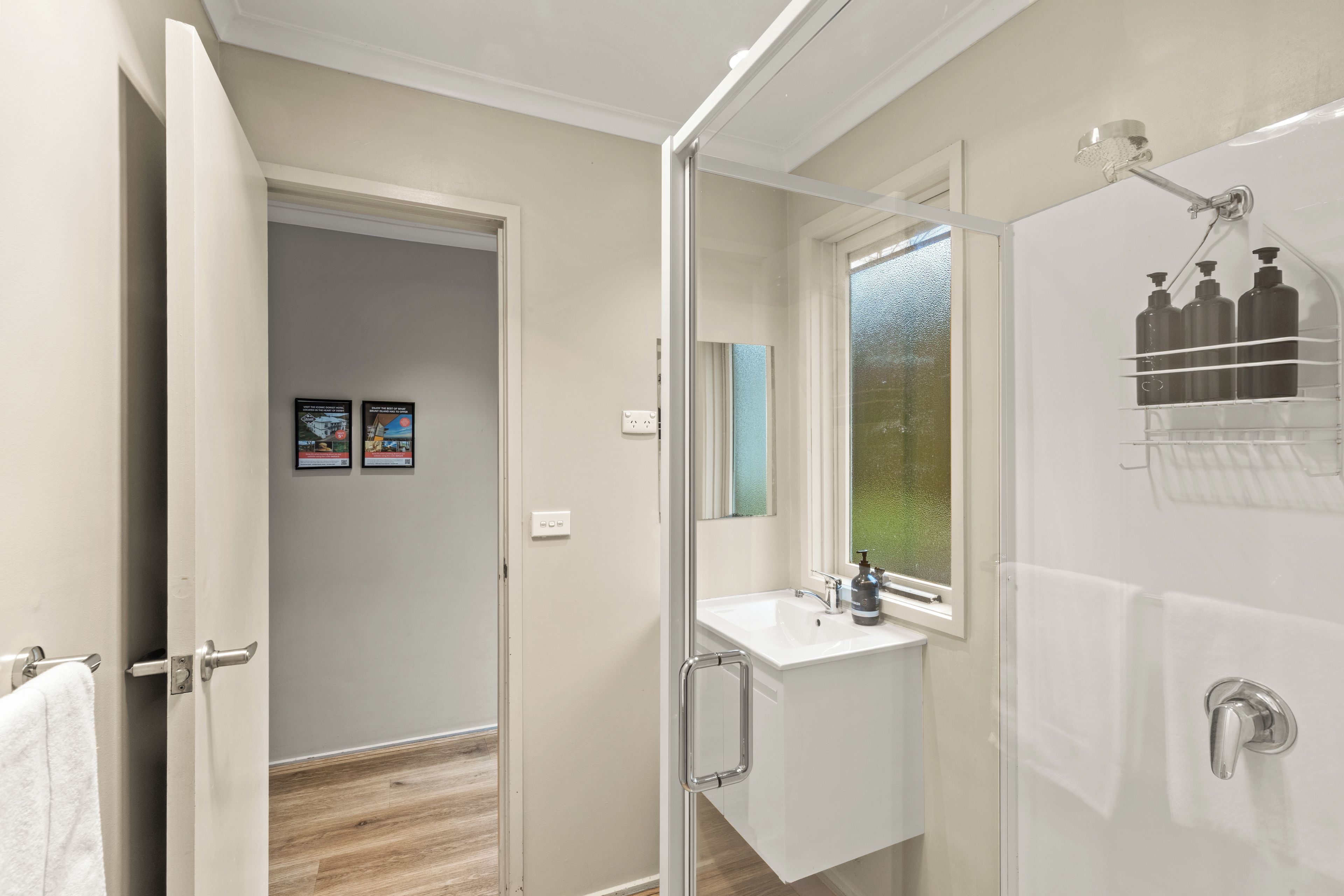 A bathroom with a shower, a sink, and a mirror. There is a towel rack and a window with a view.