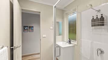 A bathroom with a shower, a sink, and a mirror. There is a towel rack and a window with a view.