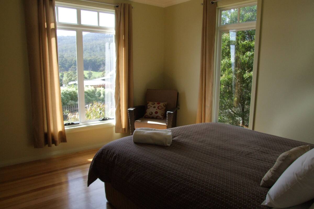 Une chambre à coucher avec un grand lit, une chaise et une fenêtre avec des rideaux.